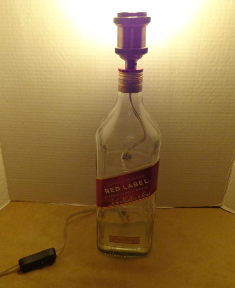 K&ouml;nnte beinhalten: Eine Lampe aus einer recycelten Glasflasche mit einem roten Etikett "John Walker & Sons Red Label". Sie hat eine kupferfarbene Lampenfassung und einen schwarzen Ein-/Ausschalter am Kabel.