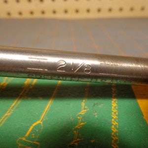 May include: A silver metal wrench with the text "2 1/8" and "COBEKI  U.S.A." engraved on the side.