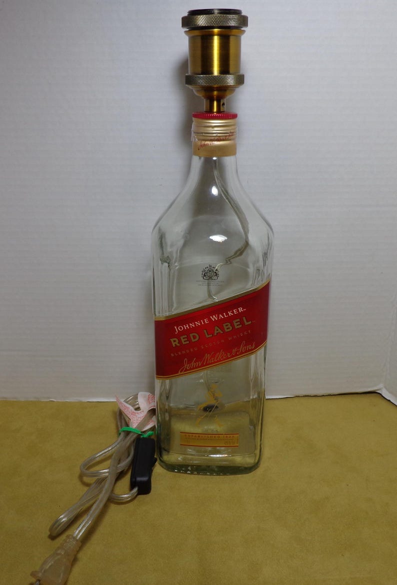 K&ouml;nnte beinhalten: Eine umfunktionierte Lampe aus einer Johnnie Walker Red Label Whiskyflasche. Die transparente Glasflasche hat ein rotes Etikett mit wei&szlig;em Text. Oben ist eine goldfarbene Lampenfassung angebracht, mit Netzkabel und Stecker.