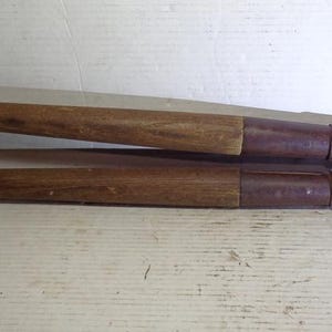 May include: A pair of vintage pruning shears with wooden handles. The shears have a metal blade and a curved cutting edge.