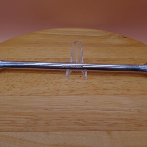 May include: A silver wrench with a blue-point label. The wrench is on a wooden surface.