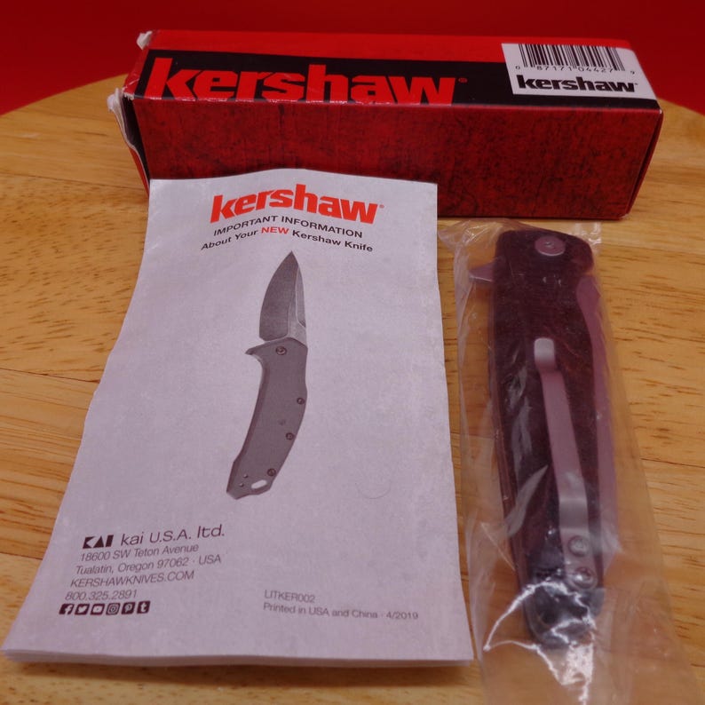 May include: A new Kershaw folding knife in a clear plastic package, next to a red and black box and a pamphlet. The pamphlet has the Kershaw logo and knife illustration. The box and pamphlet have the Kershaw brand name.