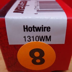 May include: A red box with the word "Hotwire" and the number "1310WM" printed on a white label. An orange sticker with the number "8" is on the front of the box. The box is on a wooden surface.
