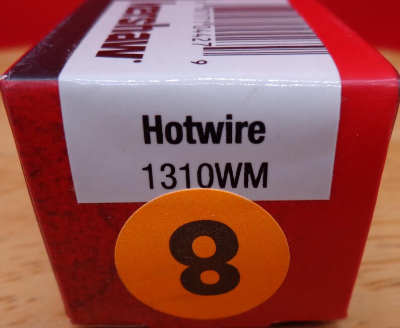 May include: A red box with the word "Hotwire" and the number "1310WM" printed on a white label. An orange sticker with the number "8" is on the front of the box. The box is on a wooden surface.