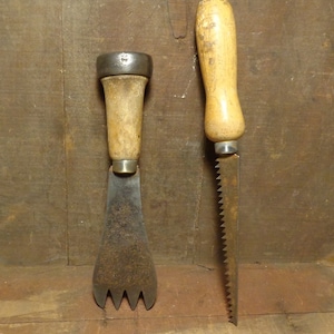 May include: Two vintage tools with wooden handles. The tool on the left has a metal blade with three prongs at the end. The tool on the right has a saw blade.