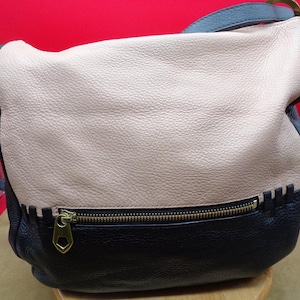 May include: A two-tone leather shoulder bag with a light tan upper section and a black lower section. The bag features a gold zipper and a black strap. The bag is a stylish accessory.
