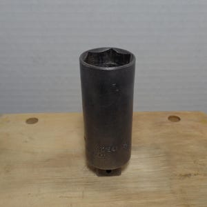 May include: A dark gray, cylindrical socket wrench with a star-shaped opening. The wrench has the number "2254" and "7/8" stamped on its side. The tool is made in the USA and sits on a light brown wooden surface.