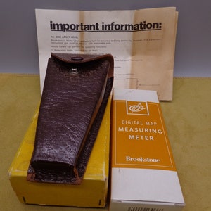 May include: A brown leather case with a metal clasp, containing a Brookstone Digital Map Measuring Meter. The meter is in a yellow and white box with the text "Digital Map Measuring Meter" and "Brookstone" printed on it.