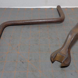 May include: Two vintage, rusty metal tools. One is a lug wrench with a socket end and a curved handle. The other is a double-ended wrench with an oval handle. Both tools are on a gray surface.