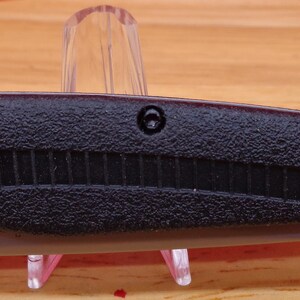 May include: A black folding knife with a textured handle and a silver blade. The knife features a gray thumb stud for easy opening and a pocket clip. The blade is partially visible, and the knife is displayed on a clear stand.