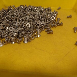 May include: A yellow plastic tray filled with a large pile of silver screws. A few screws are scattered on the tray's surface.