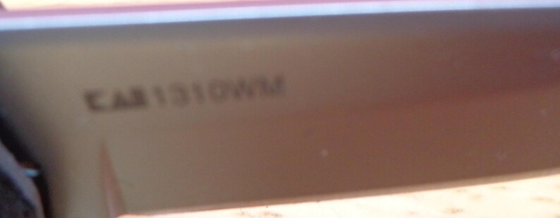 May include: A close-up of a section of a light brown object with the text "CAB1310WM" printed on it. The object appears to be a part of a larger item, possibly a piece of furniture or a vehicle component.