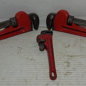 May include: Three red pipe wrenches of varying sizes are arranged on a white surface. The wrenches have a distinctive red handle and a black, adjustable jaw. The tools are designed for gripping and turning pipes.