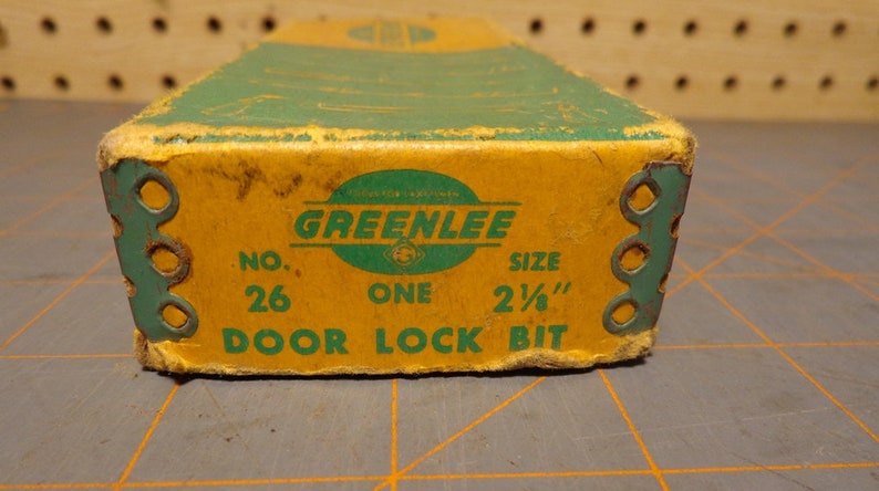 May include: A yellow and green box with the text "GREENLEE" in a green circle. The box also says "No. 26 ONE SIZE 2 1/2" DOOR LOCK BIT".