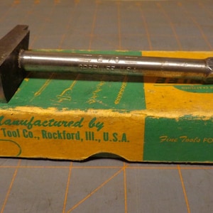 May include: A vintage metal tool with a wooden handle, labeled "Greenlee Tool Co., Rockford, Ill., U.S.A." and "Fine Tools For Craftsmen".