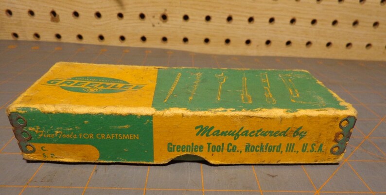 May include: A vintage Greenlee tool box with a yellow and green design. The box has the text "Fine Tools For Craftsmen" and "Manufactured by Greenlee Tool Co., Rockford, Ill., U.S.A." printed on it.