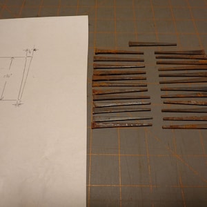 May include: A collection of 24 rusty nails, arranged in rows on a brown surface. The nails are approximately 2 inches long.