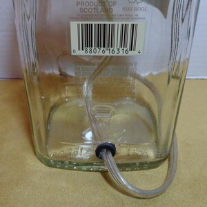 K&ouml;nnte beinhalten: Eine klare Glasflasche mit einem durch den Boden eingef&uuml;hrten, durchsichtigen Schlauch. Die Flasche hat ein Etikett mit Text und einem Barcode. Der Schlauch wird von einer schwarzen Gummit&uuml;lle gehalten. Die Flasche steht auf einer gelben Oberfl&auml;che.