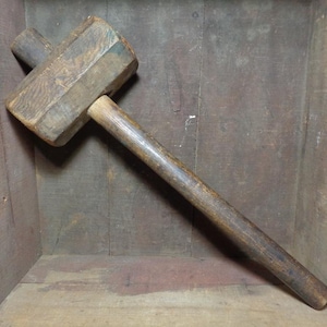 May include: A wooden mallet with a long handle. The mallet is made of dark wood and has a rectangular head.