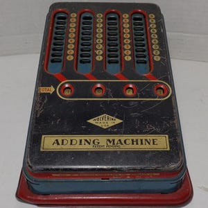 May include: A vintage black metal adding machine with red and blue accents. The machine has a total of five columns of numbers, each with a dial that can be turned to add numbers. The machine is labeled "Wolverine Adding Machine, Patent Pending".