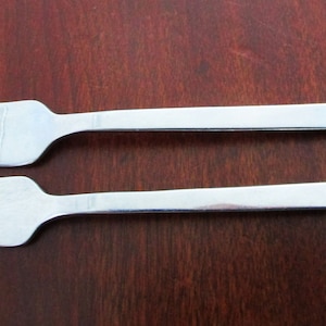 May include: Two silver forks with a brushed finish. The forks are laid out parallel to each other on a wooden surface.