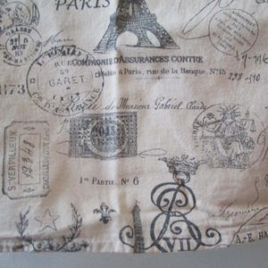 May include: A beige fabric with a black and white print of Parisian-themed stamps, including the Eiffel Tower, text, and a stamp that says "GY BARET".