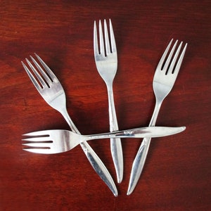 May include: Four silver forks arranged in a star shape on a dark red wooden surface.