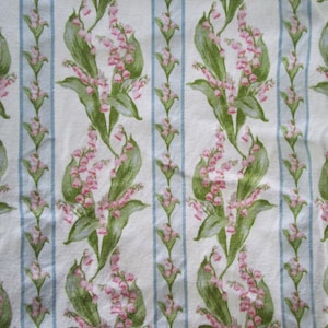 Puede incluir: Una tela con un patrón floral repetido de flores de lirio de los valles rosas y hojas verdes. El diseño se establece sobre un fondo blanco con rayas verticales de color azul claro, creando una estética botánica clásica.