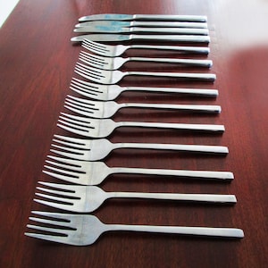 May include: A set of silverware, including forks and knives, laid out in a row on a wooden surface. The silverware is made of stainless steel and has a modern design.