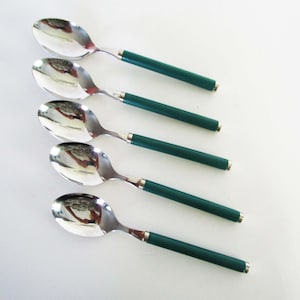 May include: A set of five stainless steel spoons arranged in a vertical row. Each spoon features a polished, reflective oval bowl and a solid, matte dark green cylindrical handle with a silver-toned metal band at the neck and base.