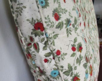 Puede incluir: Un cojín blanco con un patrón floral que presenta flores rojas, azules y verdes sobre un fondo blanco con pequeños puntos blancos. El cojín tiene un ribete blanco alrededor del borde.