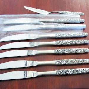 May include: Set of six silver dinner knives with ornate, engraved handles. The knives are packaged in a clear plastic bag.
