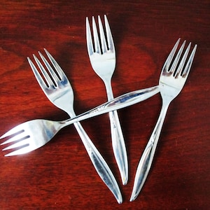 May include: Four silver forks arranged in a criss-cross pattern on a dark wood surface.