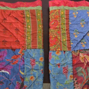 May include: Two colorful patchwork quilts with a variety of floral and geometric patterns. The quilts feature red, blue, green, and orange hues. The edges are trimmed with a red and green border.