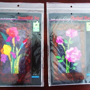 May include: Two craft pattern packets in clear plastic sleeves. The left packet is titled Irresistible Iris and features a colorful iris flower illustration. The right packet is titled Radiant Roses and features pink roses. Both include 12" x 18" text.