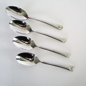 Puede incluir: Un juego de cuatro cucharas de metal plateado pulido dispuestas en una fila vertical. Cada cuchara presenta un cuenco ovalado liso y un mango delgado que termina en una punta redondeada y ligeramente ensanchada. La superficie refleja la luz.