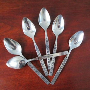 Puede incluir: Seis cucharas de plata con un diseño intrincado en el mango. Las cucharas están dispuestas en forma de abanico sobre una superficie de madera.