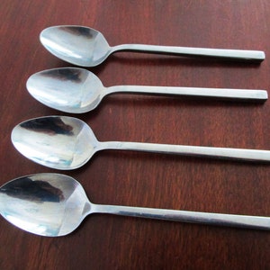 May include: Four silver spoons with rectangular handles, arranged in a row on a wooden surface.