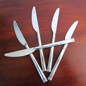 Könnte beinhalten: Fünf silberfarbene Messer mit dekorativen Griffen sind sternförmig auf einer Holzoberfläche angeordnet.
