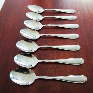 May include: Six shiny, silver spoons arranged on a dark wood surface. The spoons have a classic design with rounded bowls and long, slender handles. The spoons are reflective, showing the surrounding environment.