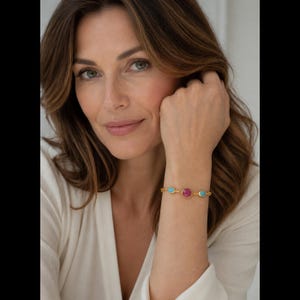 May include: A gold-toned chain bracelet featuring three circular bezel-set stones. The center stone is a deep pink, flanked by two smaller turquoise-colored stones on either side, all connected by delicate gold links.