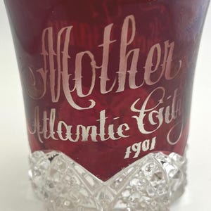 May include: A vintage, ruby-red glass with the words "Mother Atlantic City 1901" etched in a white, elegant script. The base of the glass features a cut-glass design, adding a touch of classic elegance.