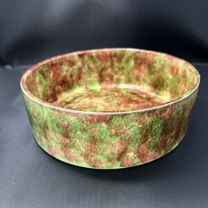 May include: A round ceramic bowl with a green and red mottled glaze. The bowl is empty and has a smooth, rounded rim.