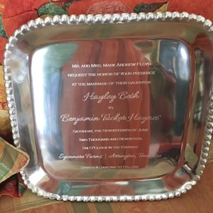 May include: A silver-colored, rectangular serving tray with a beaded edge. The tray is engraved with wedding details, including names, date, and location. The text reads "MR. AND MRS. MARK ANDREW FLOYD REQUEST THE HONOR OF YOUR PRESENCE..." and more.