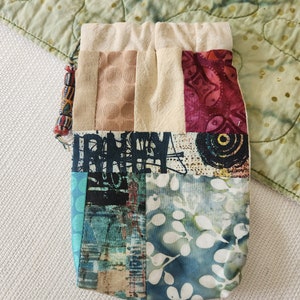 May include: A patchwork drawstring bag with a variety of colorful fabrics, including blue, green, red, and brown. The bag is made of cotton and has a natural fabric lining.