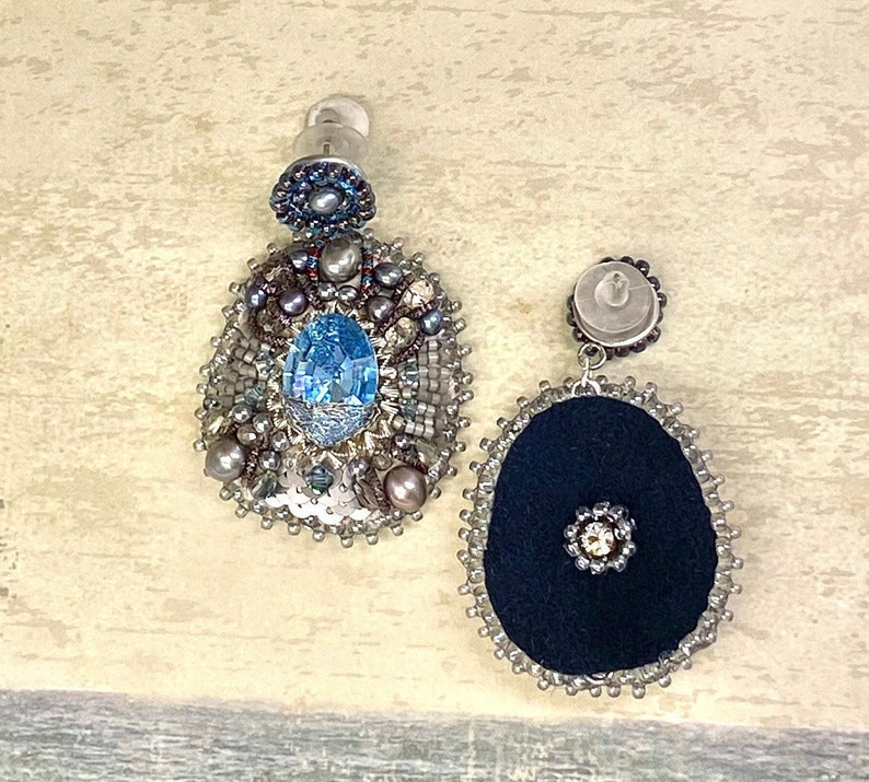 May include: A pair of dangle earrings with a blue gemstone and silver beads. One earring has a black fabric center and the other has a silver center.