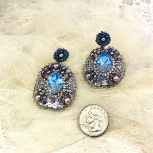 May include: A pair of silver earrings with blue crystal accents and a beaded design. The earrings are on a white background.