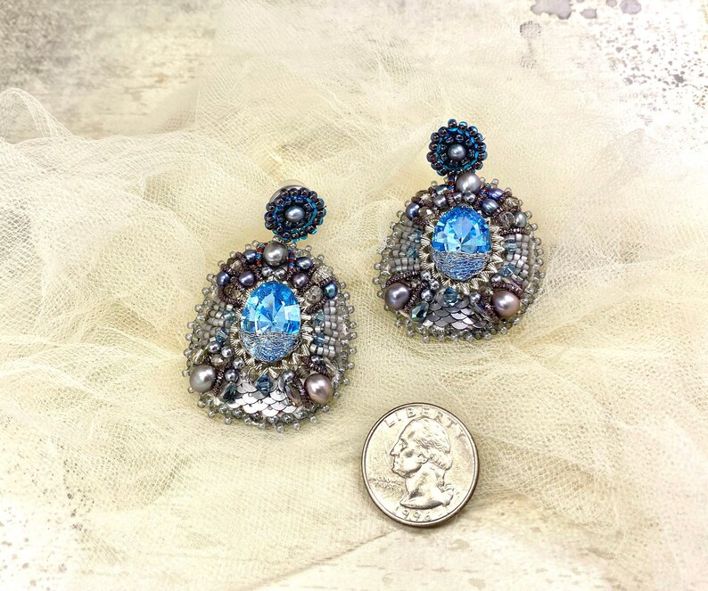 May include: A pair of silver earrings with blue crystal accents and a beaded design. The earrings are on a white background.