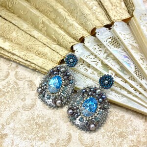 May include: A pair of silver and blue beaded earrings with a large blue crystal in the center of each earring.