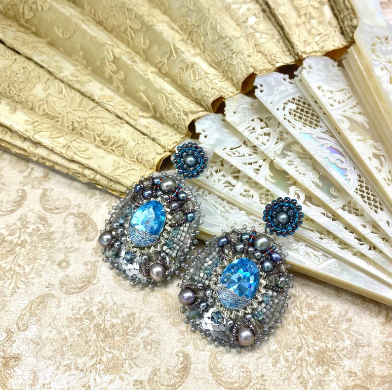 May include: A pair of silver and blue beaded earrings with a large blue crystal in the center of each earring.